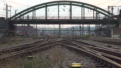 Crossing-train-tracks-at-train-station-with-cars-driving-on-bridge-in-background