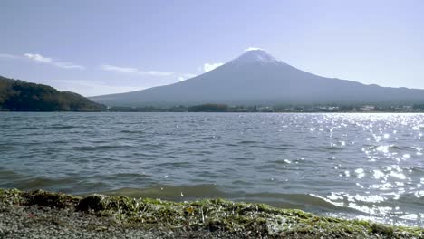 Tiefwinkelansicht-Des-Fuji-In-Der-Ferne-Mit-See-Und-Kleinen-Wellen,-Die-Sich-Im-Zeitraffer-Am-Strand-Brechen