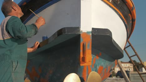 Painter-reveal-shot-of-Greek-fisherman-painting-wooden-trim-of-carvel-built-fishing-boat-slow-motion-cinematic