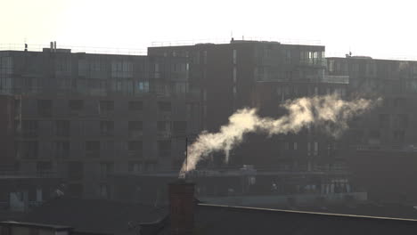 UK-October-2018--Early-morning-sunlight-catches-steam-billowing-from-a-chimney-on-an-old-school-rooftop-in-front-of-newly-built-luxury-apartments-in-East-London