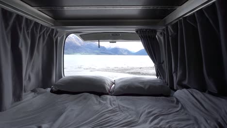 SLOWMO---Interior-of-motorhome-bed-with-pillows-and-blankets-by-Lake-Wakatipu,-Queenstown,-New-Zealand-with-snowcapped-mountains-in-background