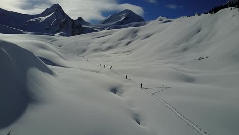 Drone-flying-over-skintrack-while-backcountry-skiers-ascend-towards-mountains
