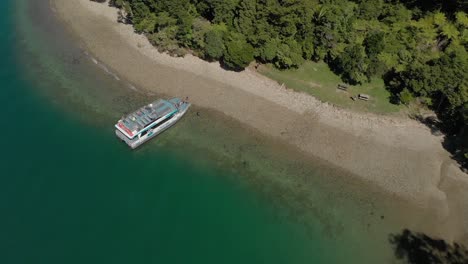 Boat-parked-on-beach-in-Marlborough-Sounds,-New-Zealand-with-crystal-clear-blue-water-and-native-forrest---Aerial-Drone