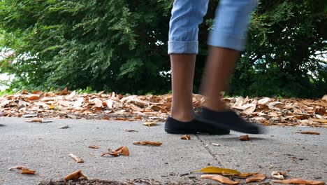 Low-angle-and-close-up-shot-of-feet-walking-by-on-a-sidewalk-surrounded-by-fallen-leaves