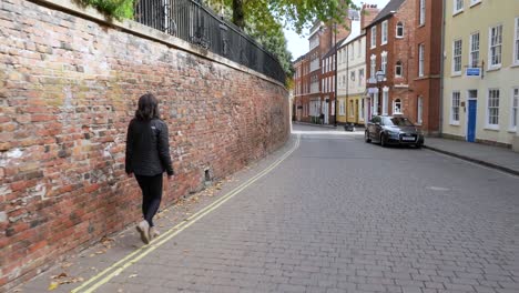 Wide-Shot-Following-an-Attractive-Young-Woman-Down-a-Cobble-Street