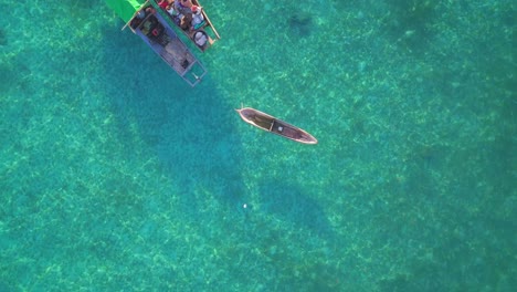 Aerial-flight-over-clear-turquoise-ocean-and-locals-on-boat-in-Mabul,-Malaysia