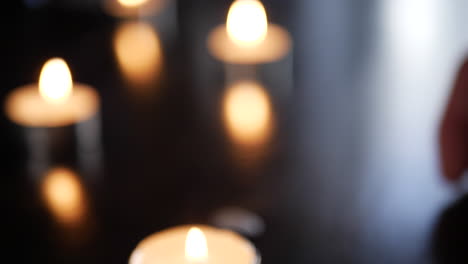 A-blurry-background-shot-with-a-hand-placing-tealight-candles-on-a-table-and-heavy-bokeh-during-a-remembrance-ceremony-or-prayer-in-church
