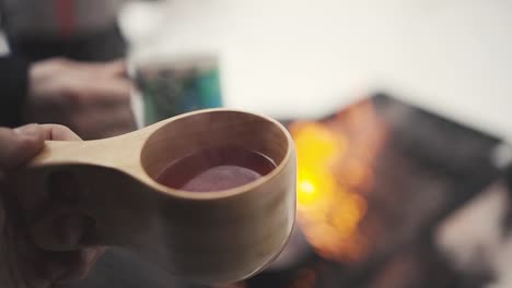 man-holding-a-wooden-cup-with-hot-beverage-in-winter-forest-in-Lemmenlaakso,-Finland