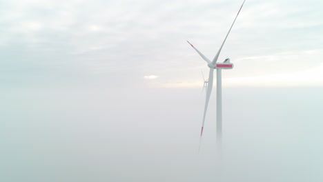 Aerial-shot-of-windmill-turbines-above-a-layer-of-dense-mist,-producing-green,-clean-energy