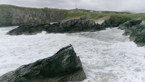 Aerial-tracking-backwards-from-a-harsh-rocky-and-sandy-coastline-on-a-windy-day