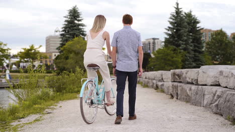 Mujer-Joven-Montando-En-Bicicleta-Con-Su-Novio-En-Un-Parque
