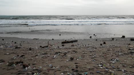 Slow-motion-tracking-shot-at-the-beach,-plastic-pollution-washing-out-from-the-ocean-at-Bali,-Indonesia
