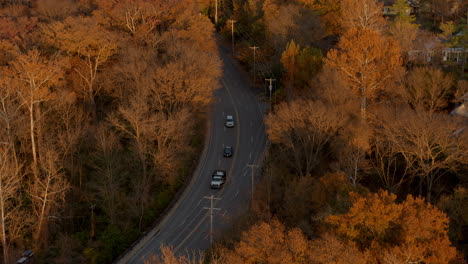 Aerial-over-a-winding-road-near-a-church-in-autumn-as-cars-drive-past-camera-tilts-down