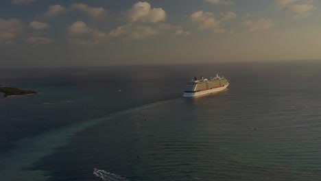 Aerial-view-of-the-cruise-ship-looking-small-sailing-into-the-big-blue-ocean-away-from-the-dock-on-the-island