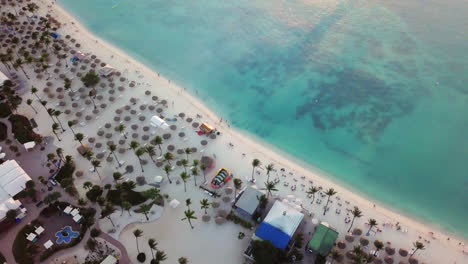 A-few-people-walk-down-the-beach-next-to-the-blue-Caribbean-Sea-in-Palm-Beach,-Aruba