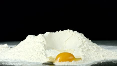 Egg-Being-Cracked-into-Some-Flour,-Against-a-Black-Background