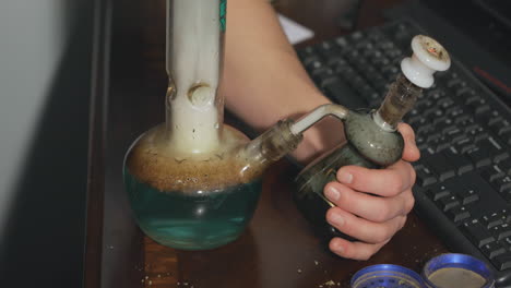 A-hand-holds-and-removes-an-ash-catcher-as-a-bowl-of-marijuana-is-smoked-on-an-office-desk