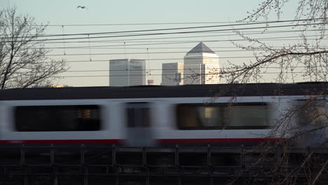 UK-February-2019--Birds-fly-over-a-train-crossing-a-bridge-with-Canary-Wharf-financial-district-in-the-background