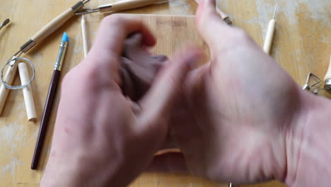 Timelapse-of-an-artist-or-sculptor-using-his-hands-and-tools-while-sculpting-a-piece-of-brown-modeling-clay-into-a-face-mask-on-a-wooden-table-in-the-art-studio-in-fast-motion