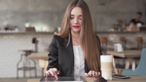 Beautiful-young-woman-listens-to-music-playing-from-her-smartphone-while-working-on-her-tablet-in-a-café