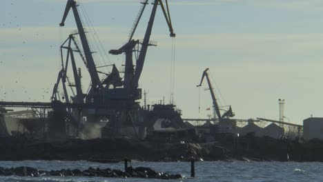 Coal-loading-in-the-Port-of-Liepaja,-working-cranes-in-the-port-in-sunny-day,-visible-sea,-wide-shot