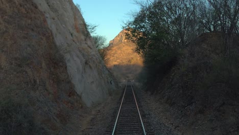 Tiro-Inclinado-Hacia-Arriba-De-Un-Ferrocarril-Y-Una-Gran-Montaña-Al-Atardecer-Desde-Un-Tren-En-Movimiento