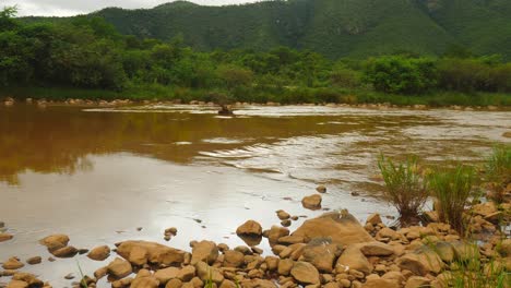 Muddy-Pongola-river-flowing-slowly-away-through-mountainous-African-landscape-with-lush-bushy-background