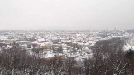 Despegue-Desde-Una-Colina-Cubierta-De-Nieve-Siguiendo-Con-Una-Vista-Panorámica-De-La-Ciudad-De-Vilnius-En-Un-Día-Nublado-De-Invierno