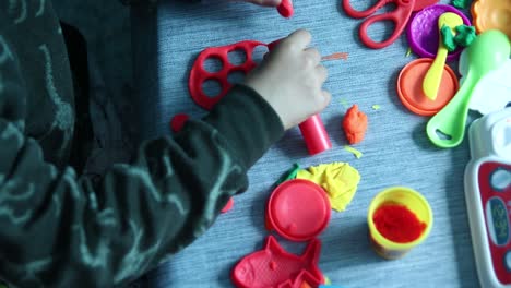 Young-boy-playing-with-colorful-non-toxic-putty-dough-plasticine-cutting-out-holes-with-tube-and-other-acessories