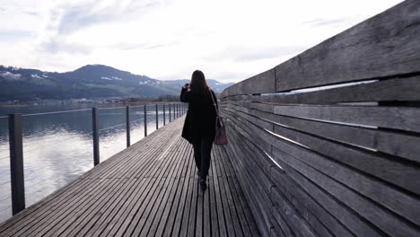 Following-shot-of-a-young-asian-woman-walking-on-a-wooden-pier-in-Rapperswil,-Switzerland-in-slow-motion