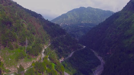 Aerial-view-of-a-curved-winding-roads-trough-the-forest-with-river,-Beautiful-nature-and-transportation-from-panoramic-view,-An-electric-pole-in-mountains