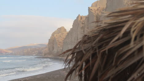 Detail-of-a-straw-beach-umbrella-with-the-black-beach-and-white-cliff-formations-in-the-background