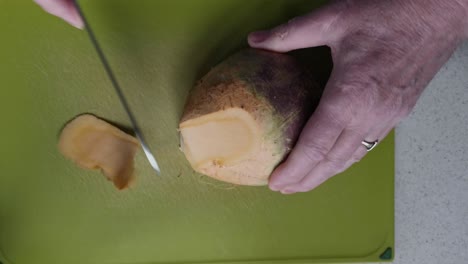 Peeling-a-large-swede-turnip-on-green-cutting-board-by-an-elderly-man