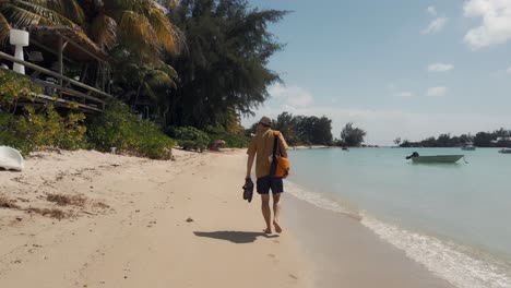 A-man-walks-barefoot-along-the-beach-with-his-shoes-in-his-hands-and-a-satchel-over-his-shoulder