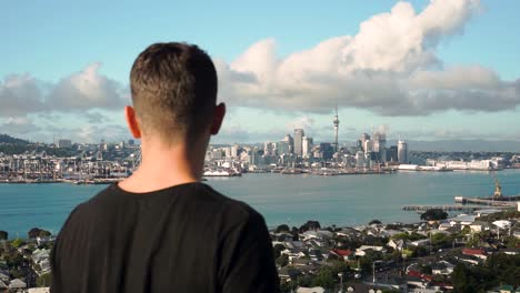 SLOWMO---Young-caucasian-man-looking-at-Auckland-skyline-from-Devonport,-New-Zealand