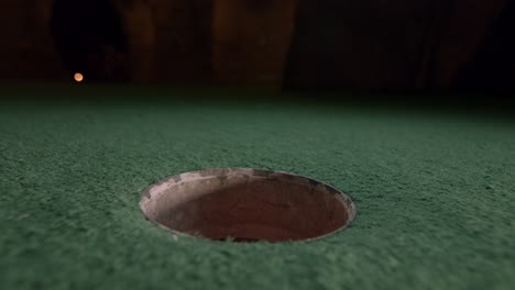 An-orange-mini-golf-ball-falls-into-the-golf-hole-and-bounces-in-the-pocket-on-a-course