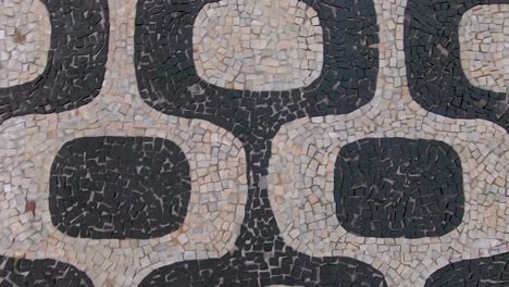 Slow-motion-forward-moving-top-down-closeup-view-of-the-so-called-Portuguese-pavement-design-in-Ipanema,-Rio-de-Janeiro,-with-typical-shapes-on-the-beach-boulevard-sidewalk