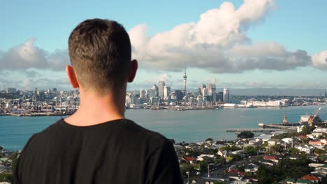 Young-caucasian-man-looking-at-Auckland-skyline-from-Devonport,-New-Zealand