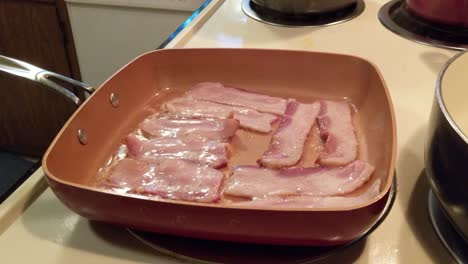 Uncured-bacon-cooking-in-a-square-pan-on-an-electric-stove