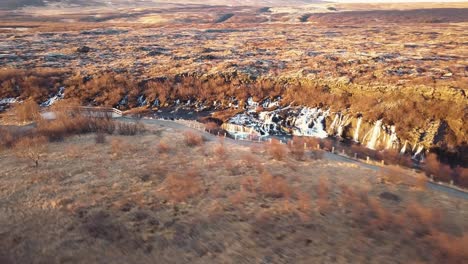 Drohne-Mit-Filmischen-Bewegungen-Zeigt-Den-Wunderschönen-Isländischen-Wasserfall-Hraunfossar-Im-Sonnenuntergangslicht-Aus-Mehreren-Winkeln