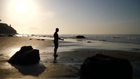 Ein-Mann-Und-Sein-Hundebegleiter-Laufen-Herum-Und-Spielen-Zusammen-Am-Strand-Bei-Sonnenaufgang-In-Santa-Barbara,-Kalifornien-Zeitlupe