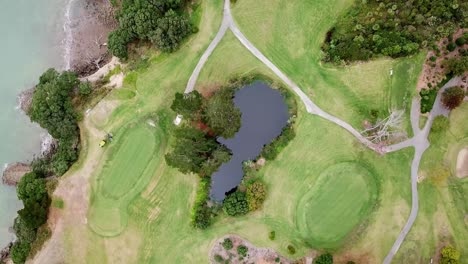 Aerial-View-of-a-Golf-course,-view-from-the-top-with-a-big-lawn-mower-running-around-in-Music-Point,-Auckland,-New-Zealand