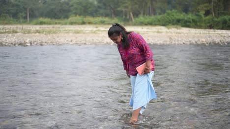 Chubby-and-healthy-young-Indian-girl-is-standing-on-small-river-bank-and-playing-with-water,-slow-motion