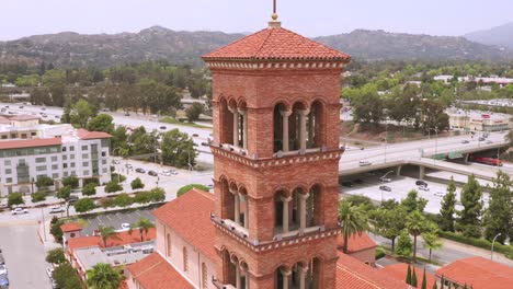 Close-up-drone-Aerial-footage,-of-St-Andrew-Catholic-Church-Clock-Bells-Tower-Landmark-of-Pasadena-City-California-With-freeway-traffic-in-the-background-on-a-cloudy-afternoon-day