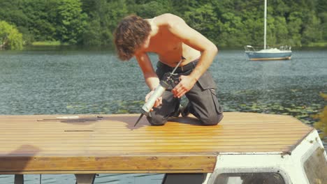 Bootswartung,-Junger-Mann-Versiegelt-Im-Sommer-Die-Dachbeplankung-Des-Alten-Holzbootes