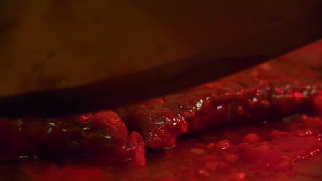 Stylistic-and-darkly-lit-macro-close-up-of-red,-bloody-meat-being-cut-by-a-knife