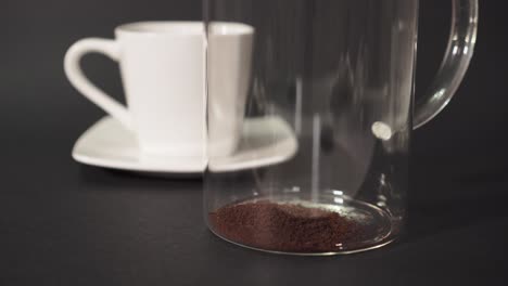 CLOSEUP---Filling-french-press-with-ground-coffee-with-white-cup-in-the-background