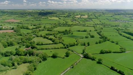 Aerial-tracking-high-along-near-a-country-back-lane-in-a-vast-green-field-landscape,-Devon,-England