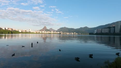 Zeitraffer-Des-Lagoa-Rodrigo-De-Freitas-Stadtsees-Mit-Sich-Schnell-Bewegenden-Wolken-über-Rio-De-Janeiro-Mit-Den-Zwei-Brüdern-Berggipfeln-Im-Hintergrund-Vor-Blauem-Himmel