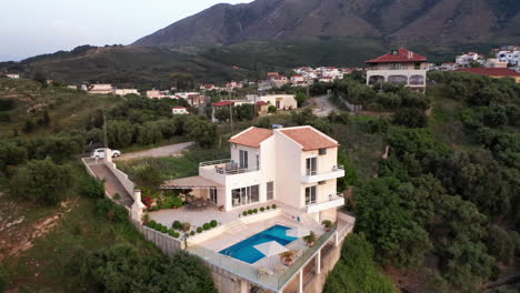 Aerial-Pull-Away-from-Luxury-Greek-Villa-with-Pool-revealing-Traditional-Greek-Village-in-Background---Car-on-Drive